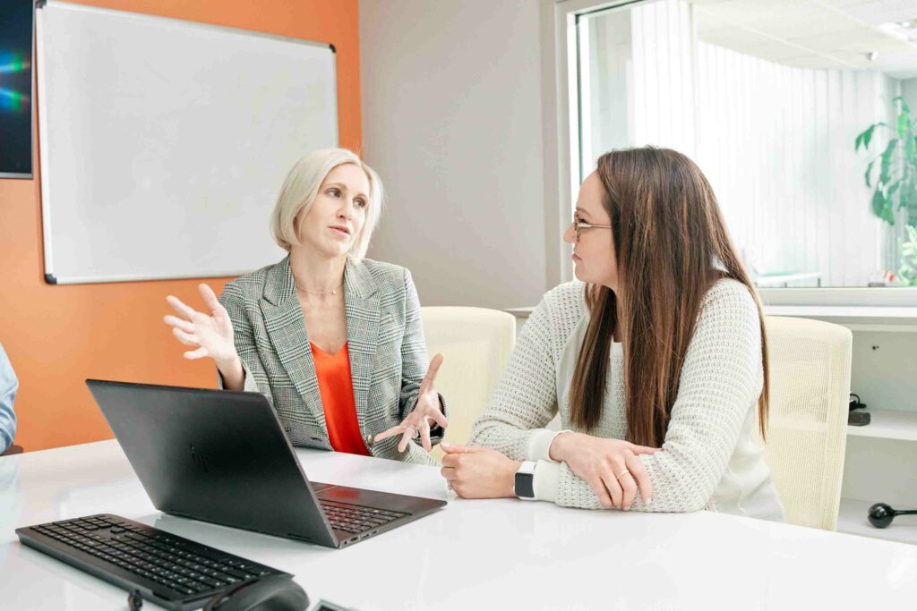 Two businesswomen engage in a focused discussion at a technology-filled office.