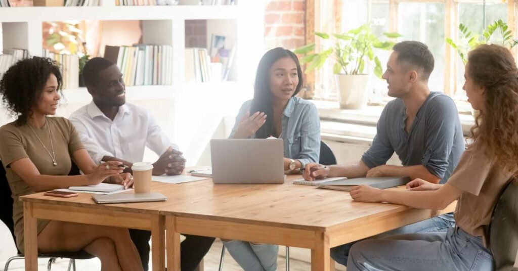 Five experts collaborate, discussing matters over a laptop in a well-lit, scholarly office.