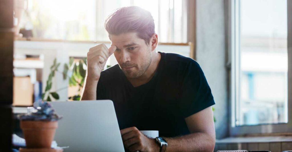 A dedicated man at a desk, studies his laptop in a bright office.