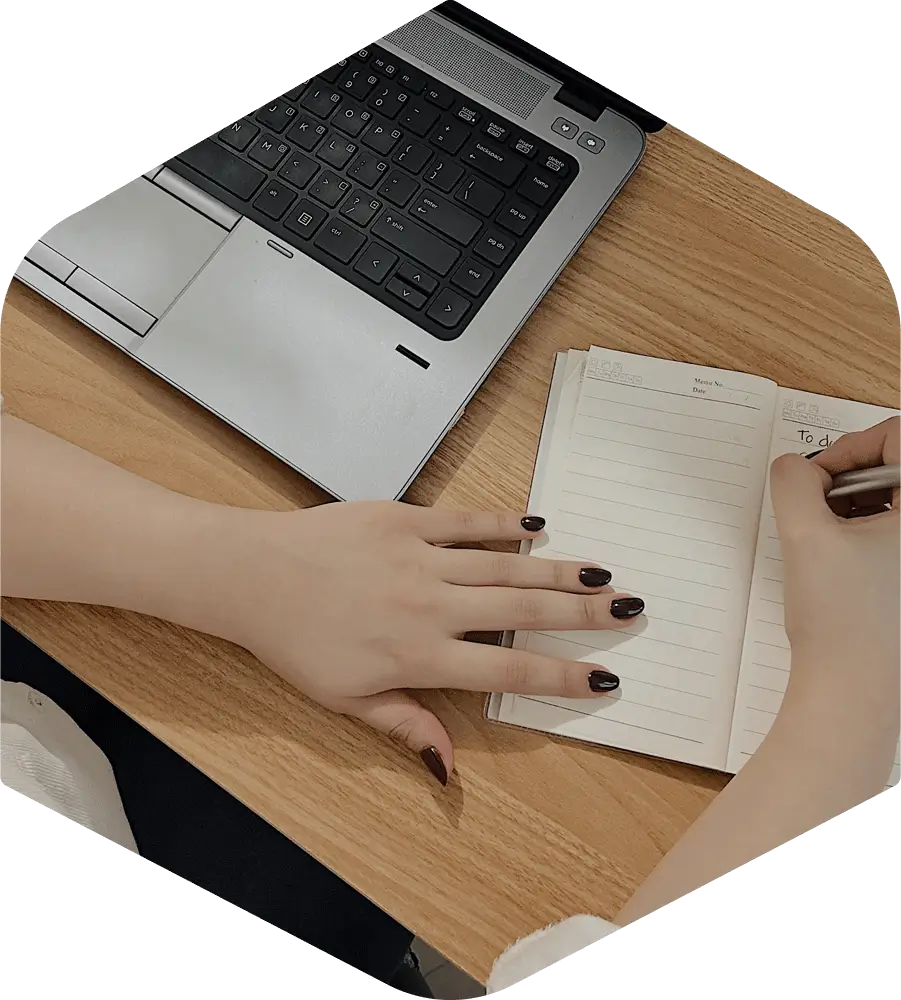 A professional prepares a to-do list beside an open laptop on a desk.